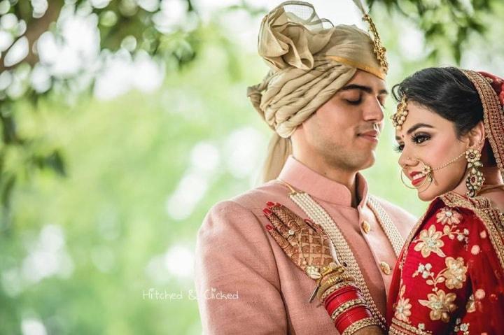 Young Indian Bride groom posing for photograph. Groom kissing the forehead  of bride. The couple is wearing traditional indian wedding dress which is  designer lehenga for bride and sherwani for groom. Stock