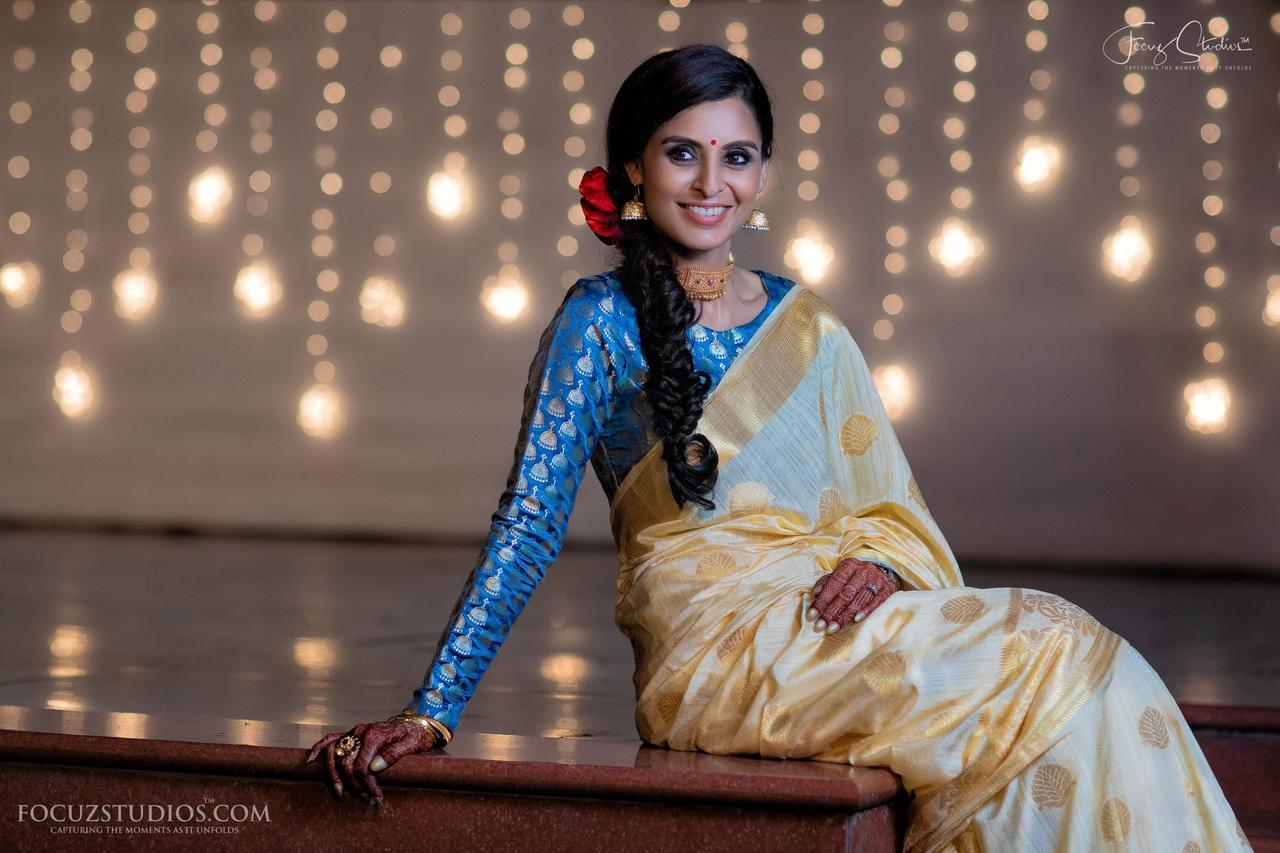 slim lady with a slight smile. She is a well pleated blue saree with tight  dark blue blouse