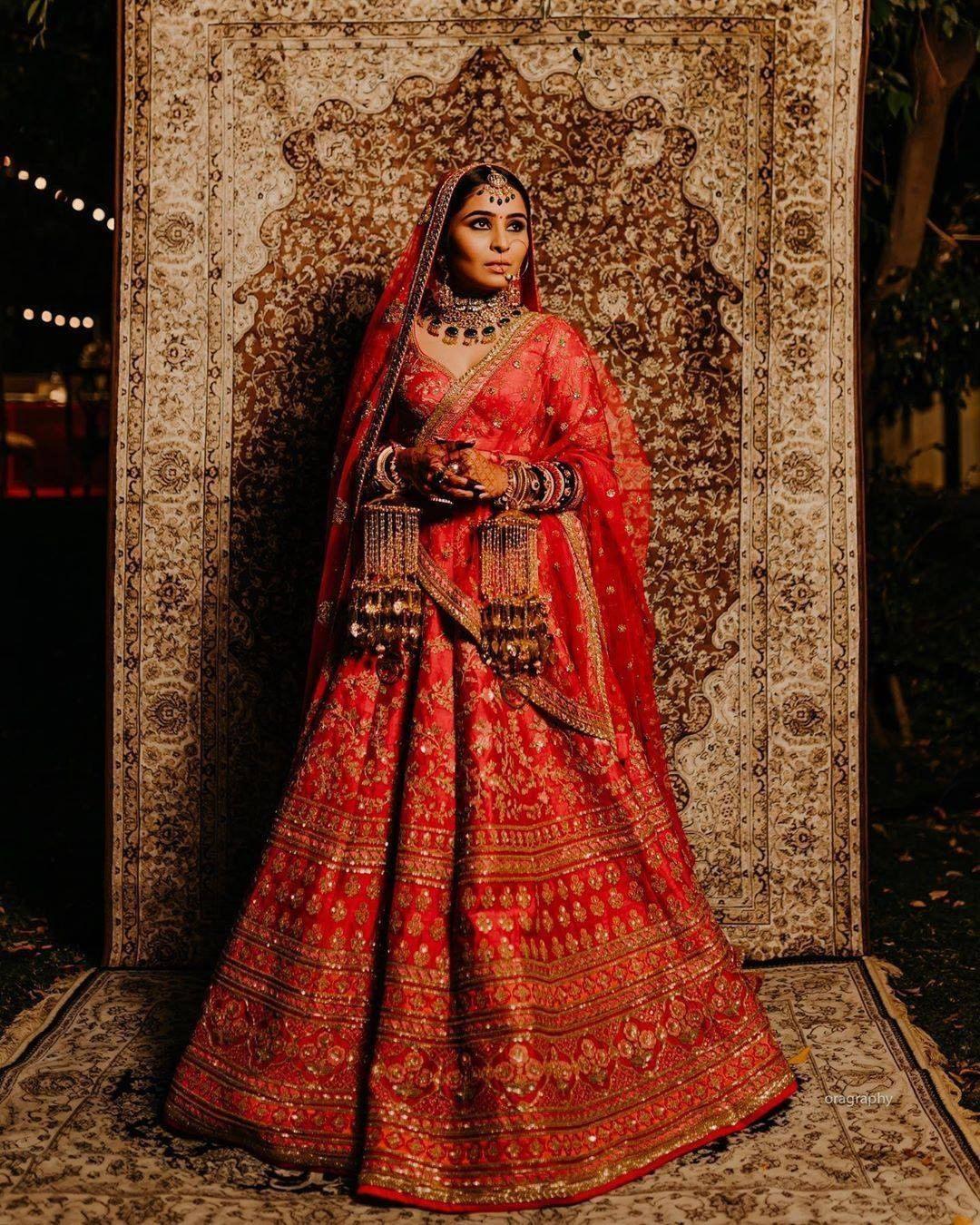 Photo of Bride wearing red bridal lehenga and green jewellery