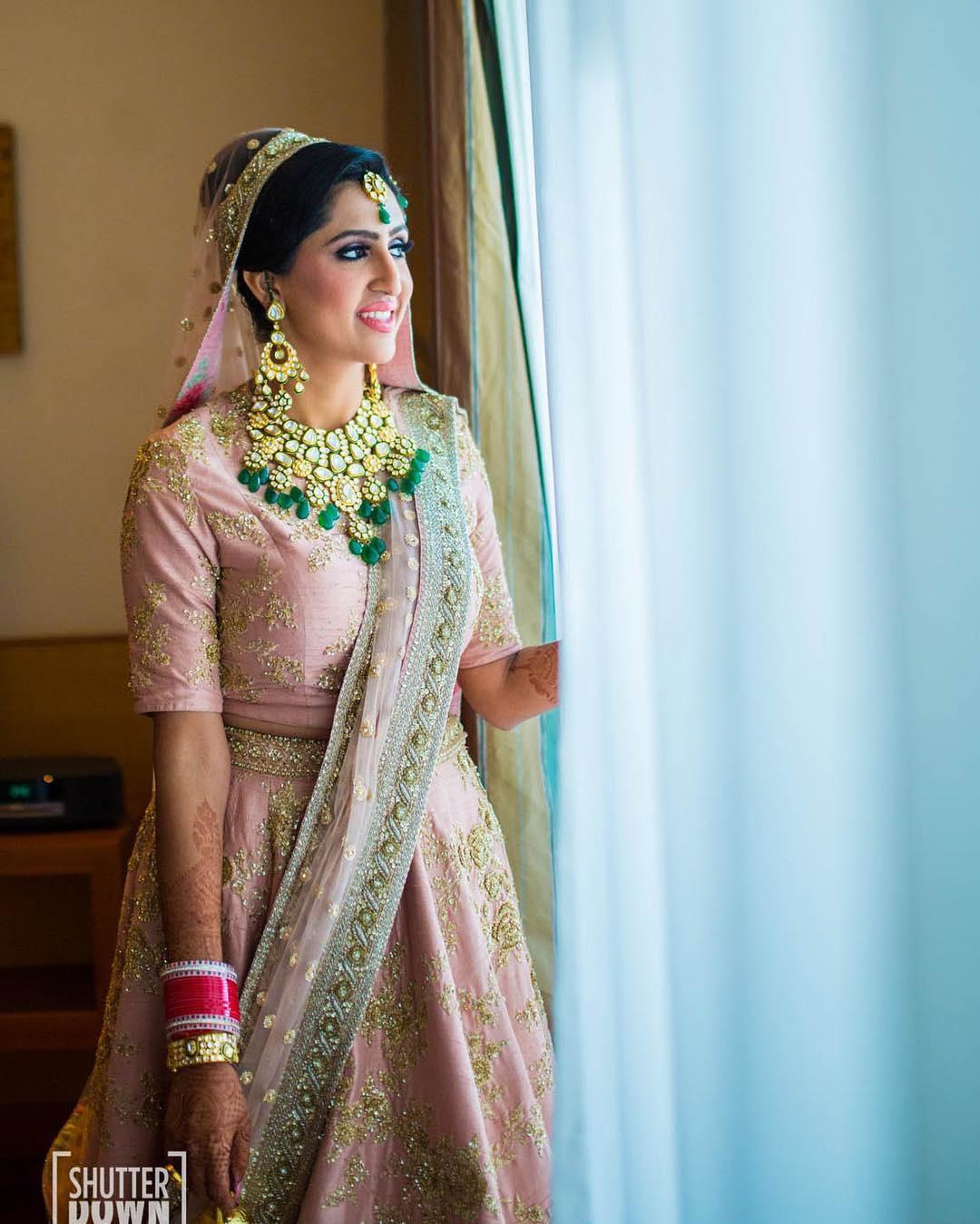 Photo of pastel pink bridal lehenga with unique blouse and green jewellery